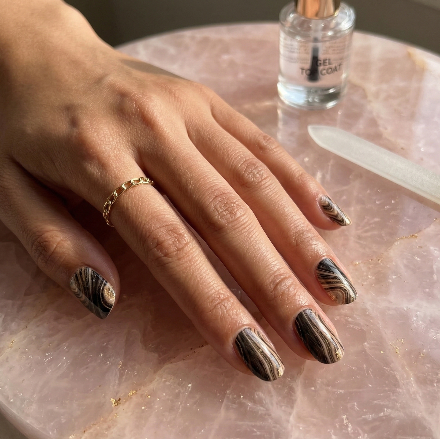 Hand with marbled nail design on a pink stone surface with a bottle of nail polish.